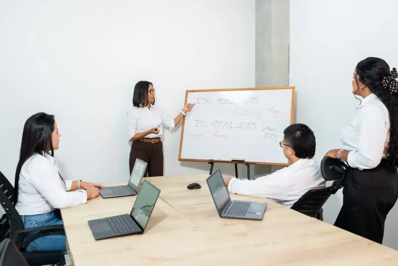 Consultora de GDE trabajando con un equipo directivo frente al tablero de normas ISO